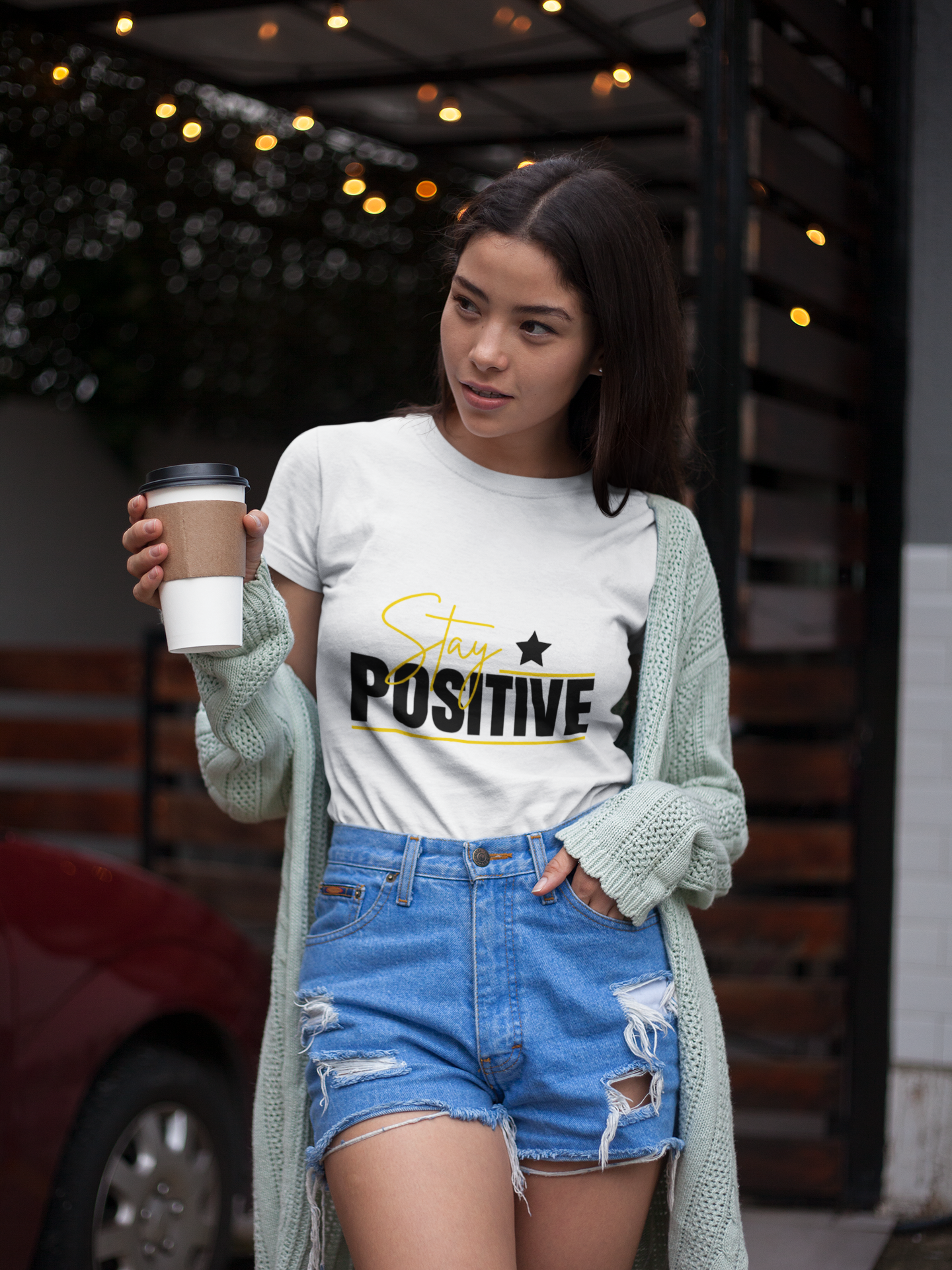 Woman wearing a 'Stay Positive' t-shirt holding a coffee cup outdoors.