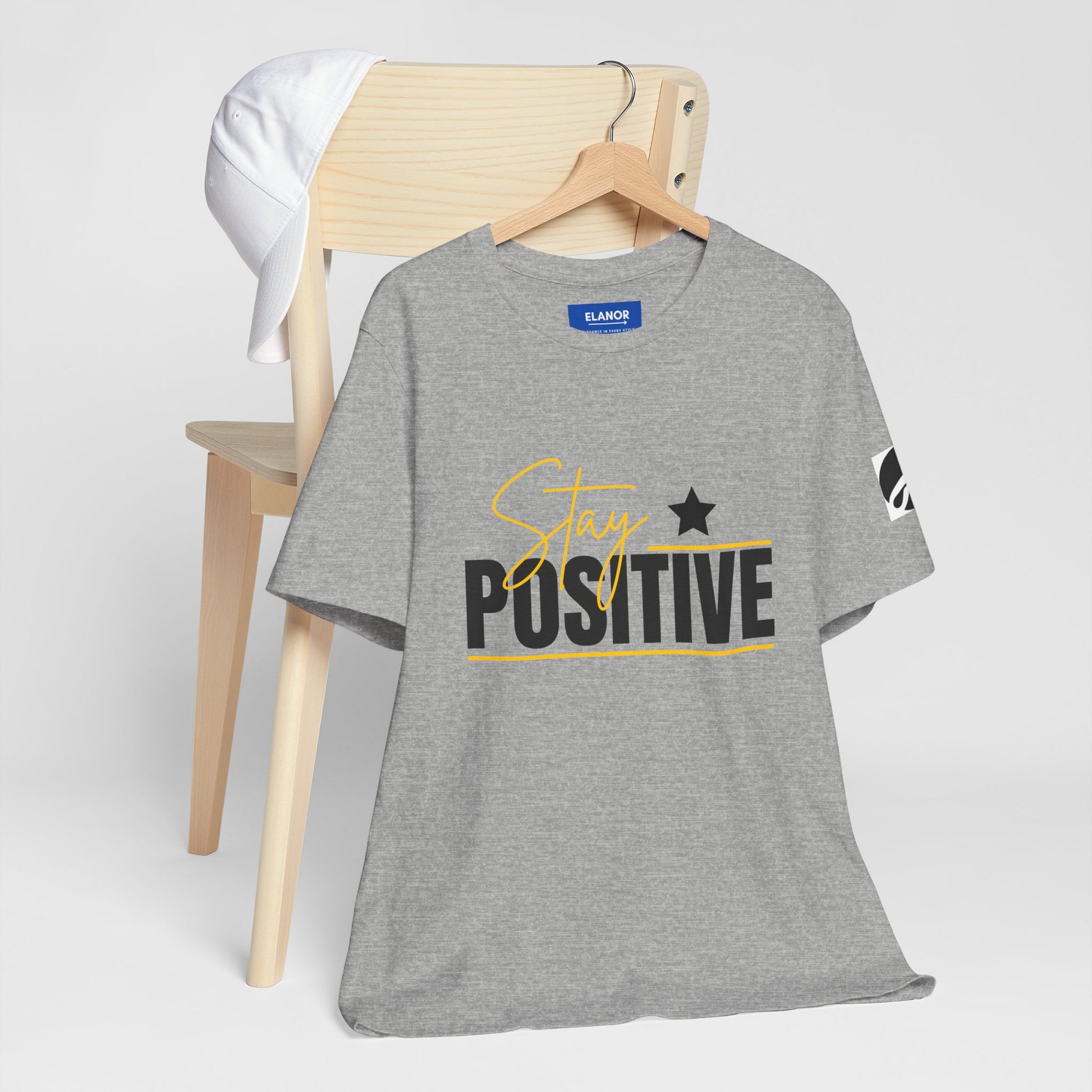 Gray t-shirt with 'Stay Positive' text on a wooden chair against a white background