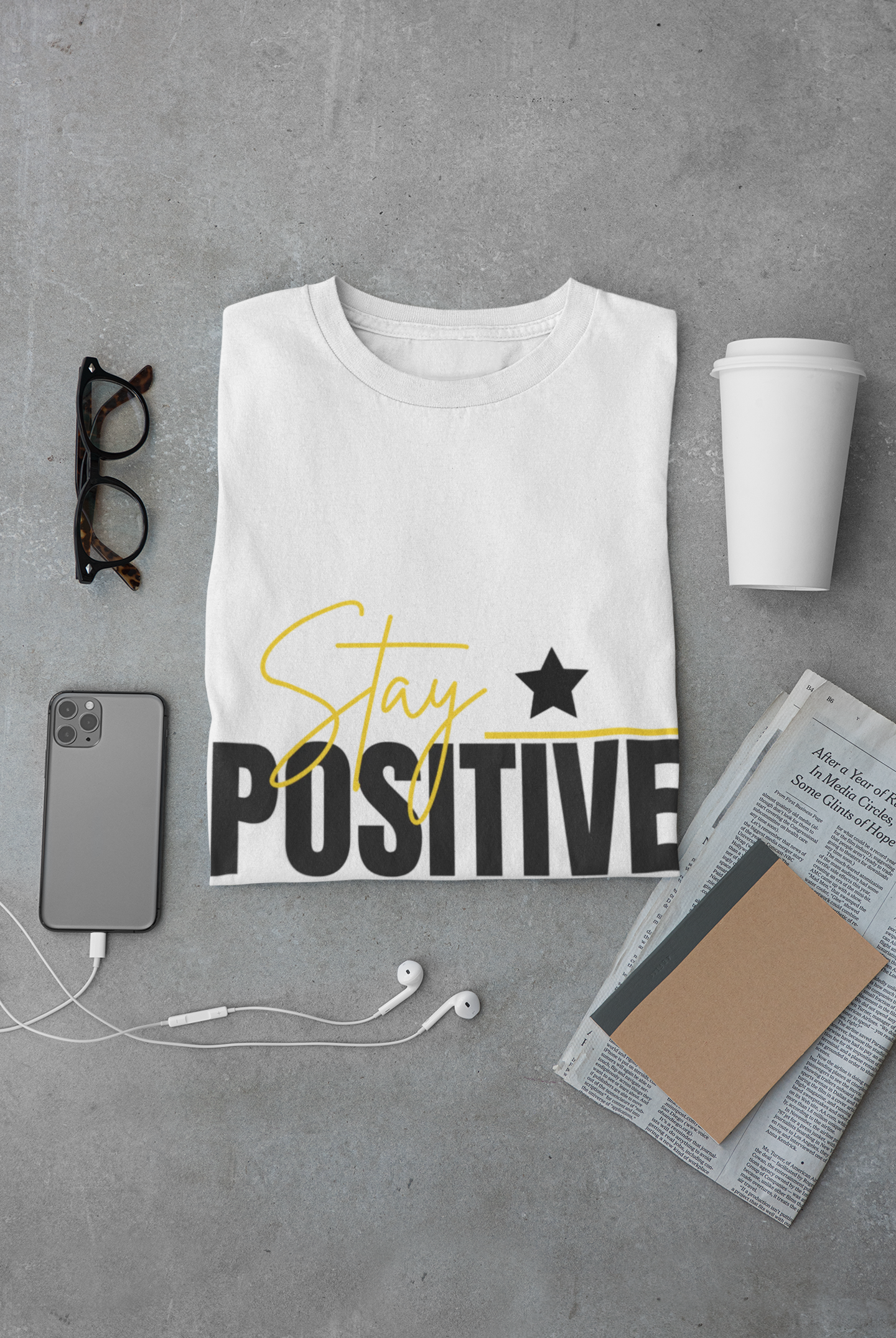 White t-shirt with 'Stay Positive' text on a gray surface with accessories.